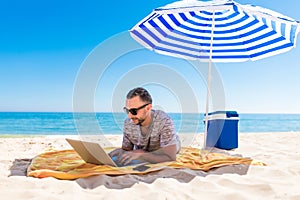 Young man using a laptop computer on the beach under solar umbrella. Freelance Concepts