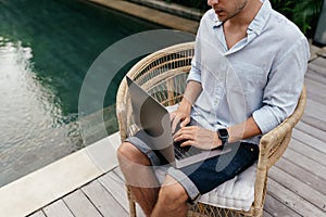 Young man using a laptop computer in a garden with a swimming pool.