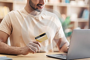 Young man using laptop and credit card while shopping online and making payment, sitting at home, closeup