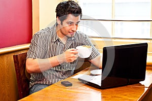 Young man using a laptop and drinking cappuccino