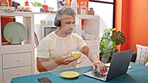 Young man using laptop and headphones drinking coffee at dinning room