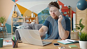 Young man using laptop in house working online and enjoying music with headphones