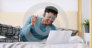 Young man using laptop and listening music on headphones in bed