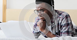 Young man using laptop and listening music on headphones in bed