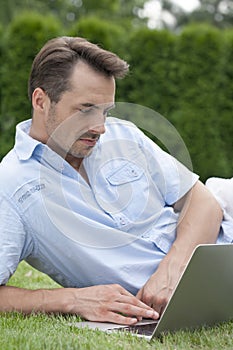 Young man using laptop while lying on grass in park