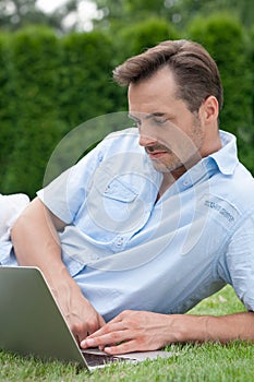 Young man using laptop while lying on grass in park