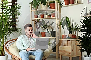 Young man using laptop in room with home plants