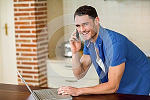 Young man using laptop and talking on phone