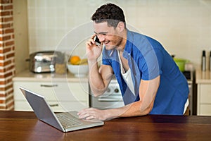 Young man using laptop and talking on phone