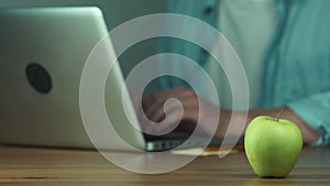 Young man using a laptop typing a message. Green apple on the table.