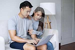 Man using laptop working online while sitting on sofa with his girlfriend together in living room. Sweet couple shopping