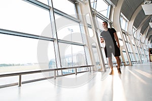 Young man using mobile phone app in airport. Young man texting smartphone walking inside office building or airport terminal