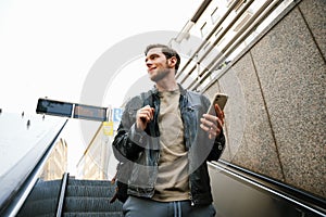 Young man using mobile phone while going down escalator outdoors