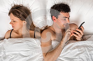 Young man using mobile phone, while his wife sleep at night