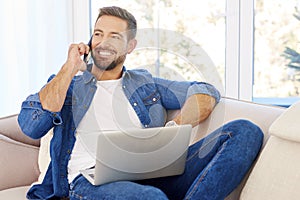 Young man using mobile phone and notebook while sitting on couch at home