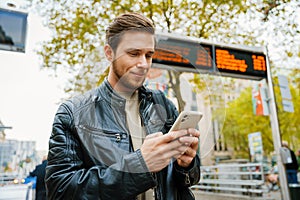 Young man using mobile phone while standing outdoors at city street