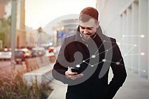 Young man using mobile phone walking along a street