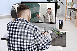 Young man using modern computer at online lesson in room, back view. E-learning