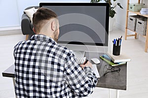 Young man using modern computer for studying at home, back view. Distance learning