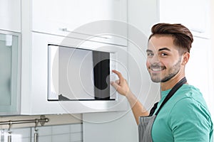 Young man using modern microwave oven