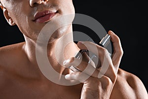 Young man using perfume on black background