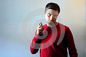 Young man using perfume or cologne on a gray background