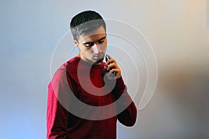 Young man using perfume or cologne on a gray background