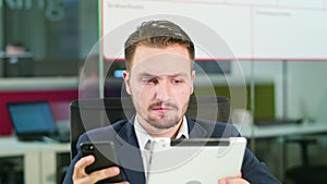 Young Man Using a Phone and a Tablet in the Office