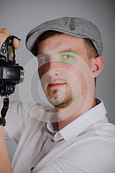 Young man using a professional camera in studio. Green box square frame autofocus on his eye. Autofocus with eye detection