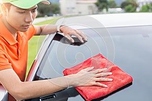 Young man using red microfiber cloth cleaning body of new silver