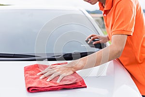 Young man using red microfiber cloth cleaning body of new silver