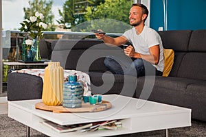 Young man using a remote control while drinking coffee on the couch