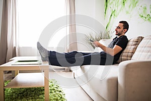 Young man using remote control while sitting on couch in living room