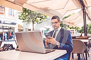 Young man using smart phone and laptop computer in street cafe