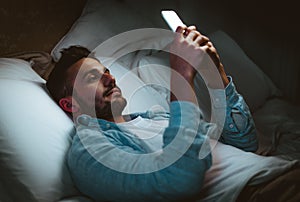 Young man using smart phone mobile - Millennial guy with cellphone lying on bed at home - Technology and people concept