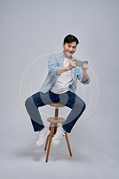 Young man using smartphone, chatting online, browsing social media, sitting on chair