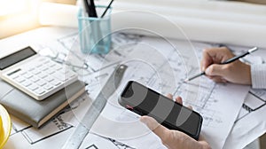 Young man using Smartphone plotting a system of building structures in blueprints