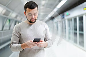 Young man using smartphone to check schedule on subway station