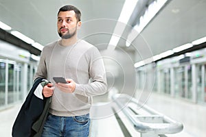 Young man using smartphone to check schedule on subway station