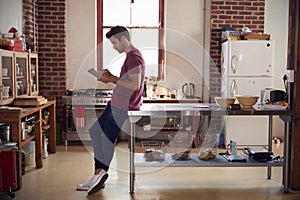 Young man using tablet computer in kitchen, full length