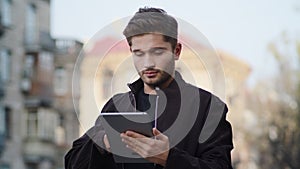 Young man using tablet outside. Hipster guy looking device screen outdoors.
