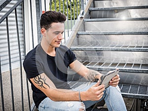 Young man using tablet PC sitting on metal stairs outside
