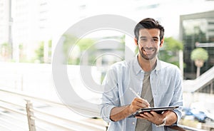 The young man using a tablet to working at out of office. The man wearing casual cloth and feeling relaxing and happy