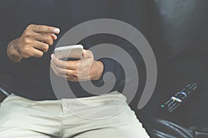 Young man using television remote control and mobile smart phone