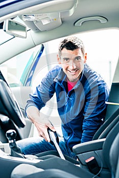 Young man using vacuum for cleaning the interior of a car