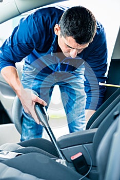 Young man using vacuum for cleaning the interior of a car