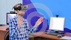 Young man using virtual reality headset in front of white blank monitor
