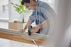 Young man using wireless drill driver to instal furniture