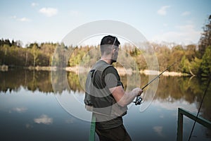 A young man in a vest is fishing on a small pond with a hunting dog. Catching fish in nature at sunset. A relaxing hobby.