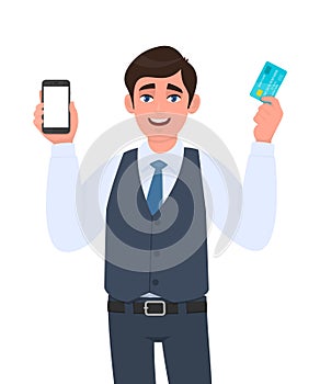 Young man in vest suit showing mobile, cell or smartphone and credit, debit, ATM card. Trendy person holding payment card.